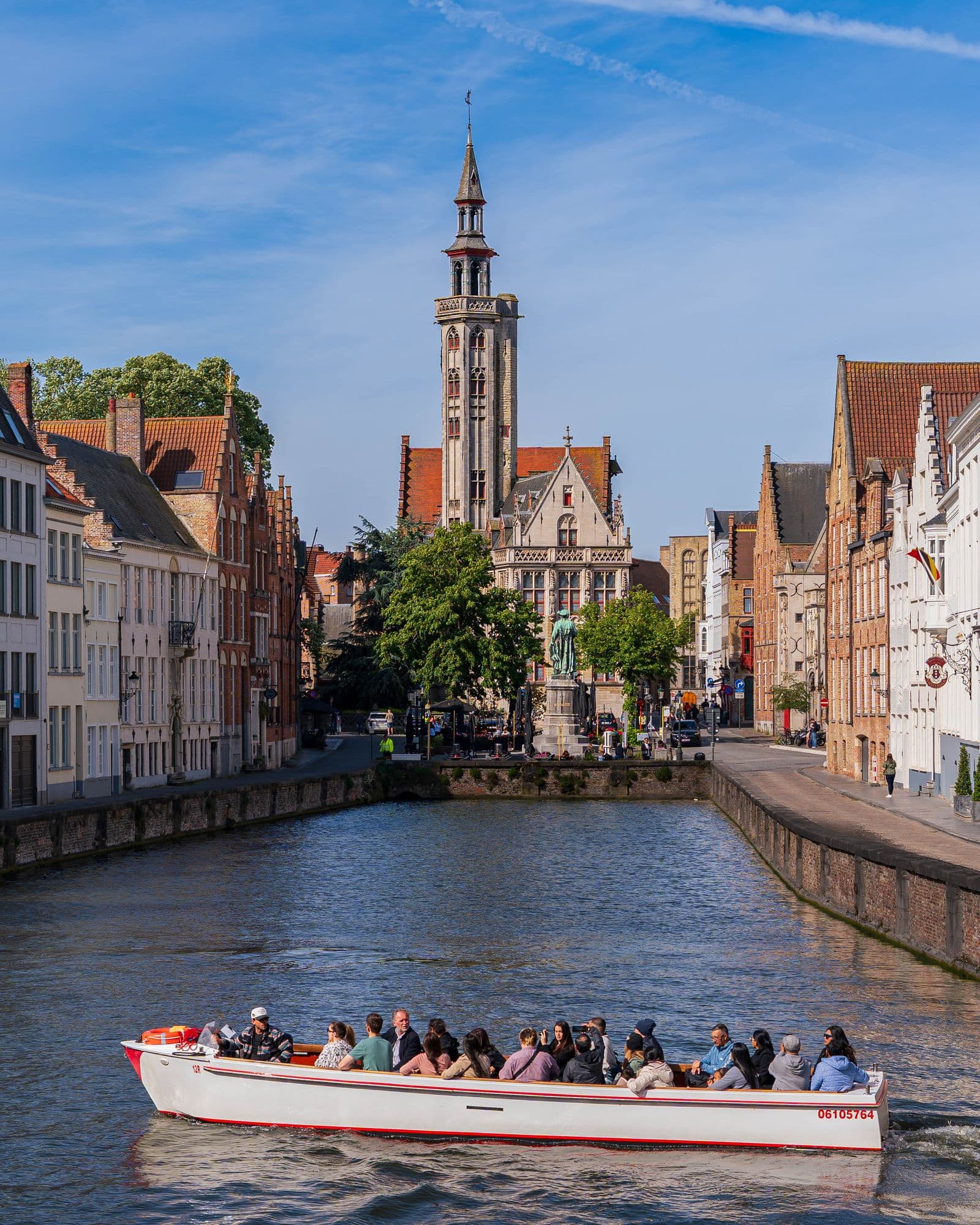Tour boat on a Bruges canal with the Poortersloge tower and gabled houses