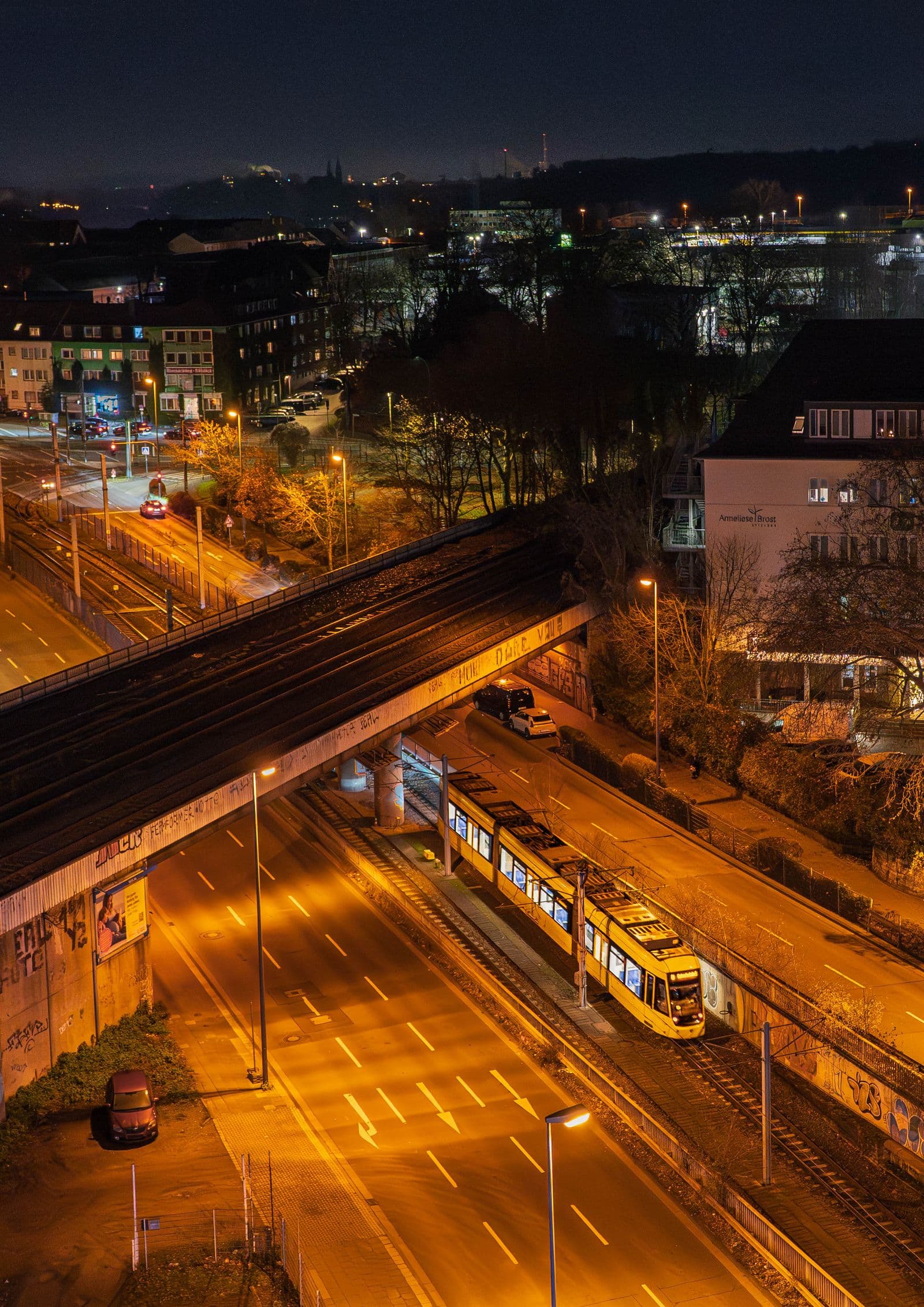 Night view from above of a yellow tram under a railway bridge in Essen, streets lit orange