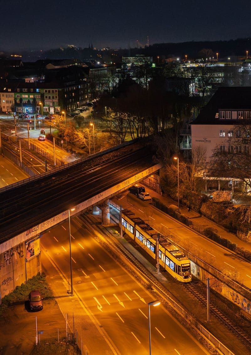 Night view from above of a yellow tram under a railway bridge in Essen, streets lit orange